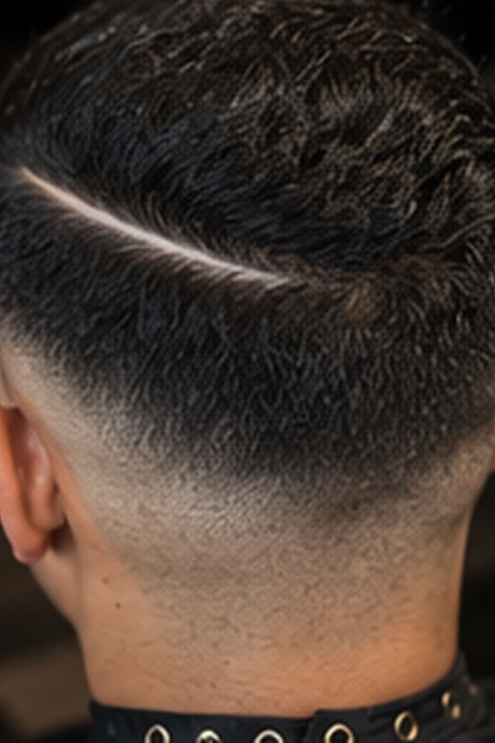 Close crop of a zero skin fade with a razored hard part, shot from behind at the nape