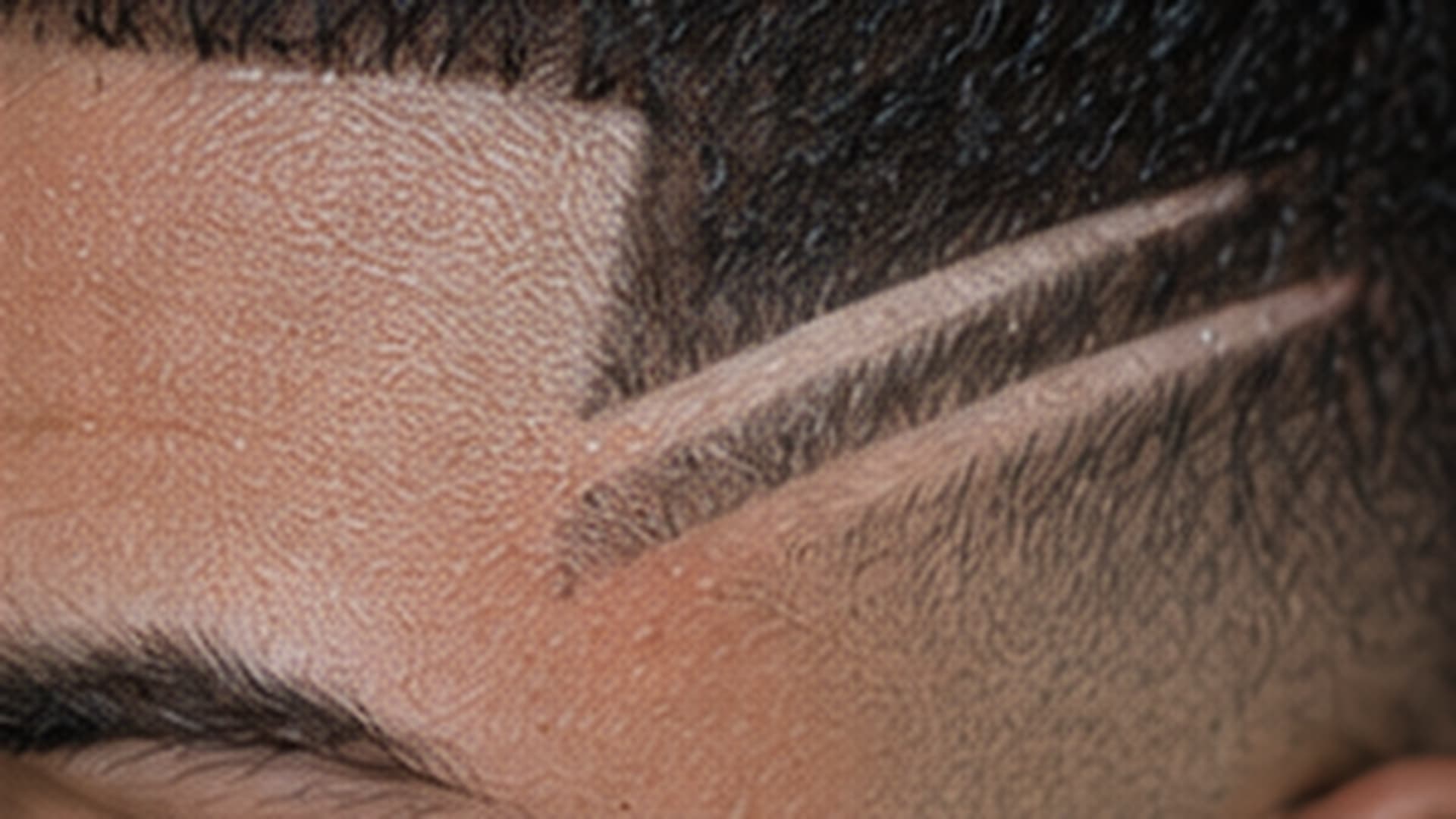 Detail of two freehand razor lines cut through a skin fade at the temple